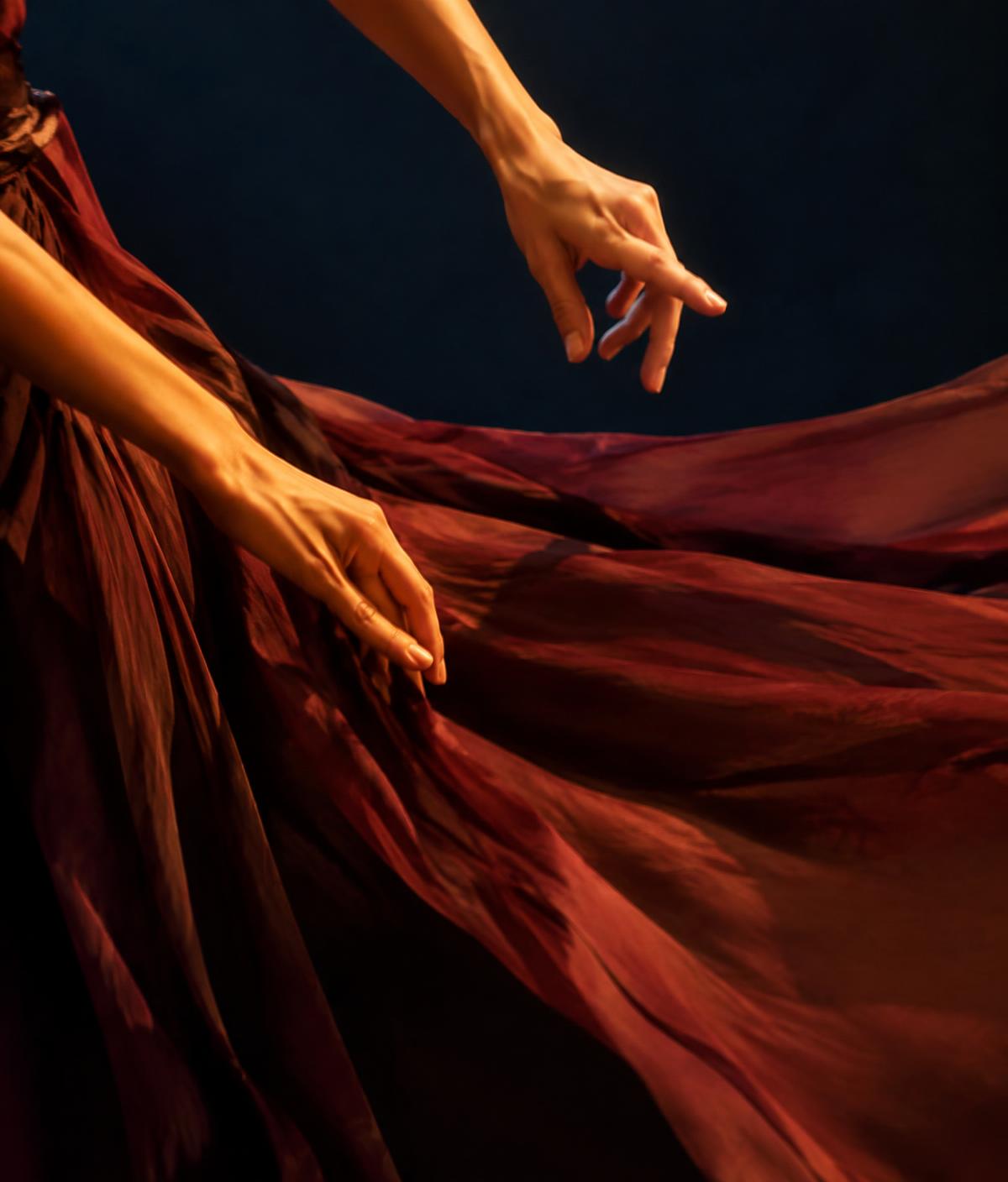 A dancer's hands moving above flowing burgundy fabric